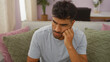 © Krakenimages.com - Young man with a thoughtful expression sitting in a cozy living room with stylish pillows and indoor plants, exuding a contemporary home atmosphere.