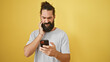 © Krakenimages.com - A perplexed young man with a beard looks at his phone against a yellow background.