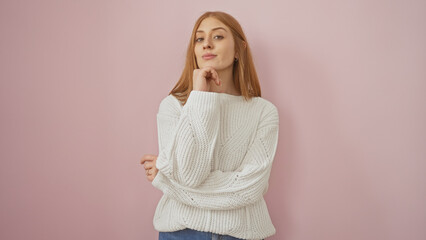 Wall Mural - A thoughtful young woman in a white sweater poses against a pink background, exuding a casual and approachable vibe.