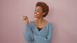 © Krakenimages.com - A cheerful african american woman in a sweater points joyfully against a pink background, embodying positivity and confidence.