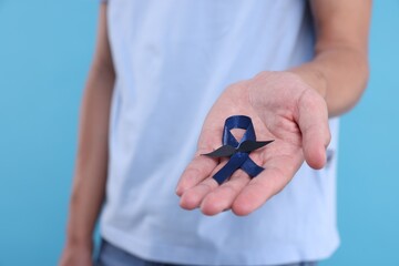 Canvas Print - Prostate cancer awareness. Man holding blue ribbon with fake mustache on color background, closeup