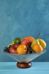 Wall Mural - Glass vase with different fresh fruits on light blue wooden table, space for text