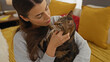 © Krakenimages.com - A young hispanic woman is tenderly holding her pet cat while sitting on a bed in a cozy bedroom.