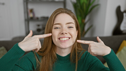 Wall Mural - A cheerful young caucasian woman pointing at her smile, in a cozy living room.