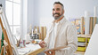 © Krakenimages.com - A bearded senior hispanic man with a gentle smile holds a palette and brush in an artist's studio, embodying creativity and experience.