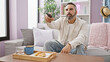 © Krakenimages.com - Mature bearded man in casual attire holding a remote in a cozy living room with a sofa and breakfast tray.