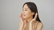 © Krakenimages.com - Young asian woman with a fresh complexion posing against a white background, touching her face gently.