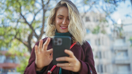 Sticker - A young blonde woman smiling while using a smartphone in a sunny outdoor park setting