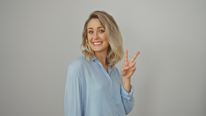 Poster - A cheerful blonde woman in a blue shirt making a peace sign against a white background.