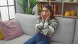© Krakenimages.com - Surprised young hispanic woman sitting on a gray sofa indoors with a shocked expression and modern decor