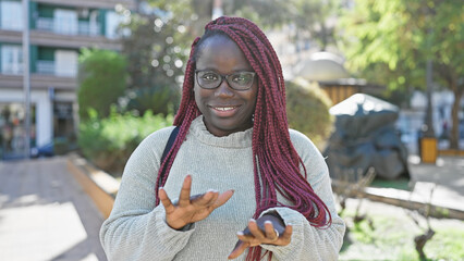 Poster - Smiling african woman with braids wearing glasses outdoor in a city park.