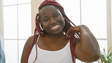 Poster - A cheerful african american woman with red braids posing indoors in a bright living room