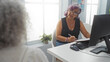 © Krakenimages.com - Woman talking to another woman at an office desk, discussing paperwork, in a professional indoor setting with a computer and natural light