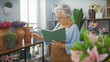 © Krakenimages.com - Senior woman reads a book inside a vibrant flower shop surrounded by colorful blooms and greenery.