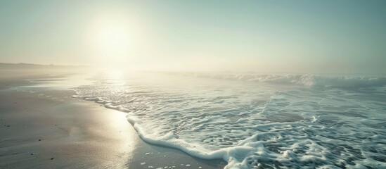 Poster - Misty morning sun shining above a sandy ocean shore with waves providing a clear view in the distance for a copy space image