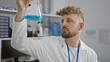 © Krakenimages.com - A young caucasian man with blue eyes and a beard examines a flask in a laboratory setting.