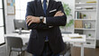 © Krakenimages.com - Confident man in a suit stands with crossed arms in a modern office, exuding professionalism and executive presence.