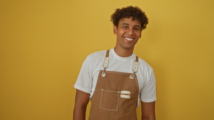 Young hispanic man smiling over isolated yellow background wearing a white shirt and brown apron