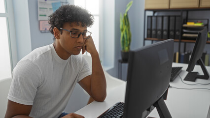 Young man focused on computer work in a bright, modern office adorned with plants and organized shelves.