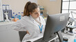 © Krakenimages.com - A young hispanic woman in a lab coat suffers back pain while working on a computer in a laboratory setting