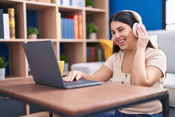 Canvas Print - Young beautiful hispanic woman listening to music sitting on floor at home