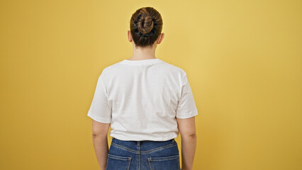 young beautiful hispanic woman standing backwards over isolated yellow background