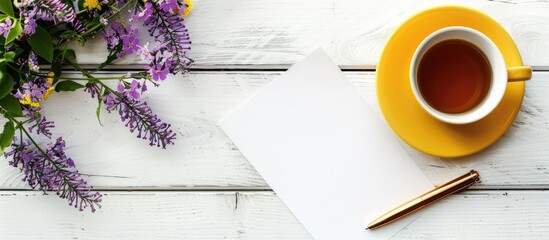 Sticker - White wooden background with a blank sheet of paper pen tea filled yellow mug stationery and purple flowers Features space for text alongside a copy space image