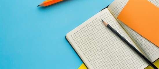 Wall Mural - Top view of an open notebook with a black pencil orange candles and a perforated sheet of paper on a blue yellow background with copy space image