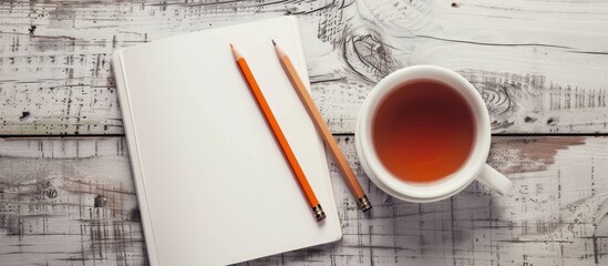 Poster - From above a notebook with blank white paper pencils and a cup of tea on a table with a copy space image is visible