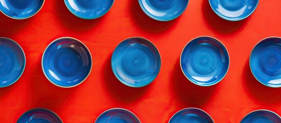Leinwandbilder - Top view of a striking pattern of blue plates on a vibrant red backdrop with ample copy space image
