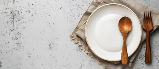 Wall Mural - Rustic vintage dining set with a wooden spoon fork and white plate on a napkin made from water hyacinth against a light gray concrete background with an empty plate perfect for a copy space image in