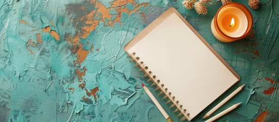 Fototapete - Top down view on a turquoise textured background with blank notepaper wax pencils and a candle offering ample space for text
