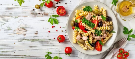 Aufkleber - Top view of a fusilli pasta salad with tuna tomatoes olives and parsley on a white wooden backdrop featuring copy space for images