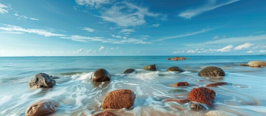 Wall Mural - Two large boulders in shallow blue ocean water long exposure image. with copy space image. Place for adding text or design