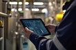 © arhendrix - Engineer using a tablet to monitor industrial machinery operation in a factory setting, focusing on control panel graphics and processes.