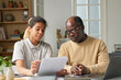 © Mediaphotos - Portrait of young woman and senior man discussing project details in a modern home office, surrounded by books and office supplies, with light streaming through large windows