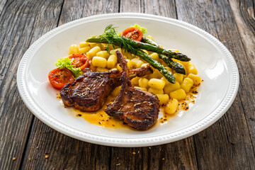 Sticker - Lamb chops with bone, gnocchi and cooked green asparagus served on white plate on wooden table 