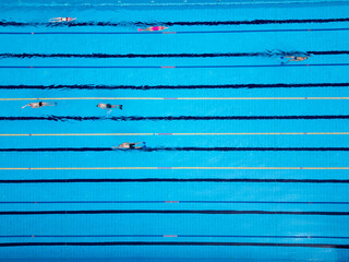 Drone video of swimmers in a clear blue pool, captured from above. The top-down view emphasizes the rhythmic motion of the swimmers and the vibrant, refreshing atmosphere of the water