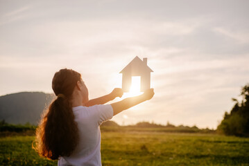 Cute little girl kid holding paper house standing in fields at amazing sunset sun village. Pretty kid hold home model dream buying real estate investment mortgage bank loan insurance concept