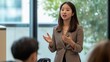 © fotofabrika - Woman presenting in a professional setting surrounded by an engaged audience during a daytime business meeting