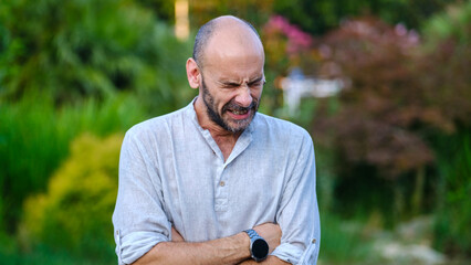 Wall Mural - A middle-aged handsome businessman in a tree-lined park on a summer day, looking at the camera while yawning with a tired expression