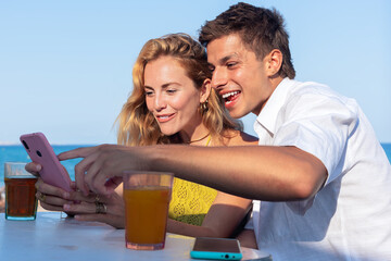 smiling woman and man enjoying vacation in a restaurant. Beautiful and cheerful Generation Z girls browsing the internet with smartphones