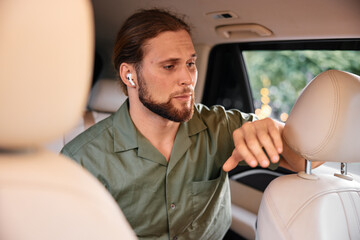 Wall Mural - Young man with earbuds in car looking thoughtful