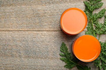 Wall Mural - Healthy carrot juice in glasses and green leaves on wooden table, top view. Space for text