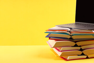 Wall Mural - Stack of colorful books and laptop on yellow background, space for text