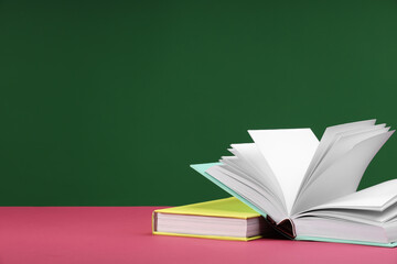 Wall Mural - Colorful books on pink table against green background, space for text