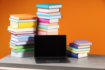 Wall Mural - Stacks of colorful books and laptop on wooden table against orange background