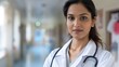 © nopommajun - A focused female doctor wearing a white coat with a stethoscope stands confidently in a hospital corridor, conveying professionalism and compassion.