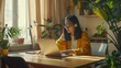 © VK Studio - A young woman in a cozy room works on her laptop, surrounded by houseplants and warm sunlight streaming through the window.