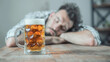 © Bonsales - Man resting his head on table with full beer mug in focus, background blurred. Indoor setting suggests relaxation or fatigue after a long day